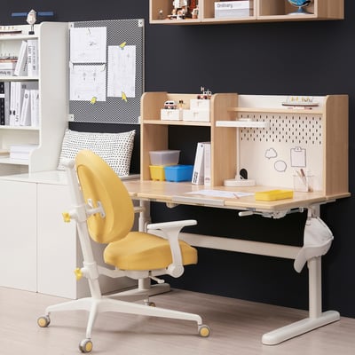 A GUNRIK kids chair in yellow and white. Its adjustable, comfy, and versatile. Positioned under a wooden desk, surrounded by storage shelves.