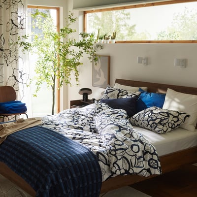 A bed with a HÄRLIR blue and white floral duvet cover set, made from recycled cotton and lyocell, positioned centrally and prominently in the room.