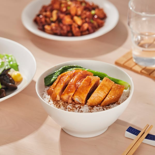 White bowl holds chicken, rice, and greens. Chopsticks rest beside, ready for meal.
