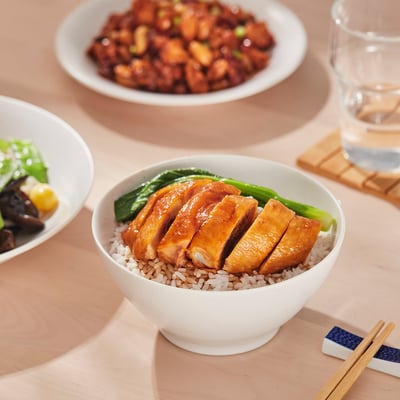 White bowl holds chicken, rice, and greens. Chopsticks rest beside, ready for meal.