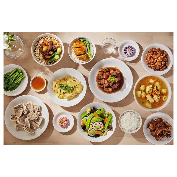 Top view of various asian dishes on white plates and bowls, including noodles, rice, dumplings, and vegetables, arranged neatly on a wooden table.