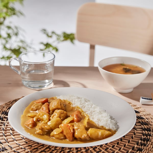 Porcelain bowl with yellow curry chicken, rice, and soup next to water on placemat.