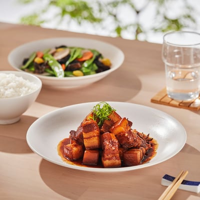Table setting with multiple bowls filled with rice, vegetables, and meat; chopsticks and a glass of water are placed on either side.