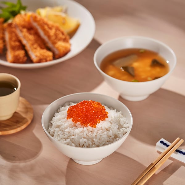 White bowls with rice, soup, and tempura on a wooden table, showcasing HARMYNTAs stackability and light weight.