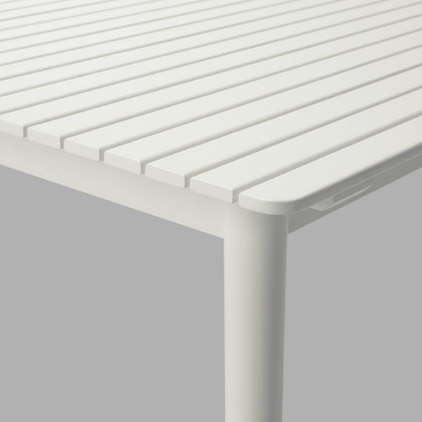 A close-up of a modern, white extendable dining table made from solid eucalyptus. The tables edge groove details, and the leg appears sturdy.