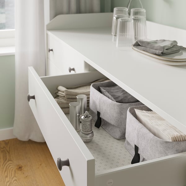 Organized white HAUGA chest drawer in kitchen. Contains bins with napkins, utensils, and containers. Clean, modern, and practical storage.
