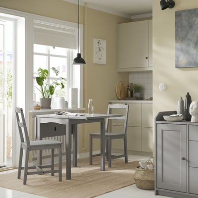 Small modern kitchen with gray HAUGA 3-in-1 drop-leaf table, two chairs, beige floor, windows, beige cabinets, and decor.