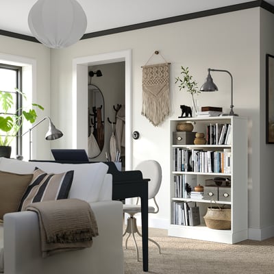 Bright living space with modern decor: white sofa, gray chair, wooden bookshelf with books, plants, and a black lamp.