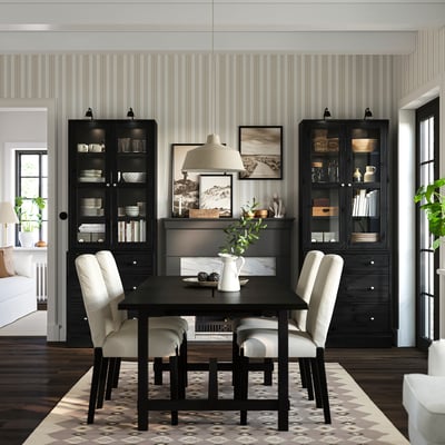 Modern dining area with black HAVSTA table, glass cabinet, pendant lamp, striped walls, and patterned rug.