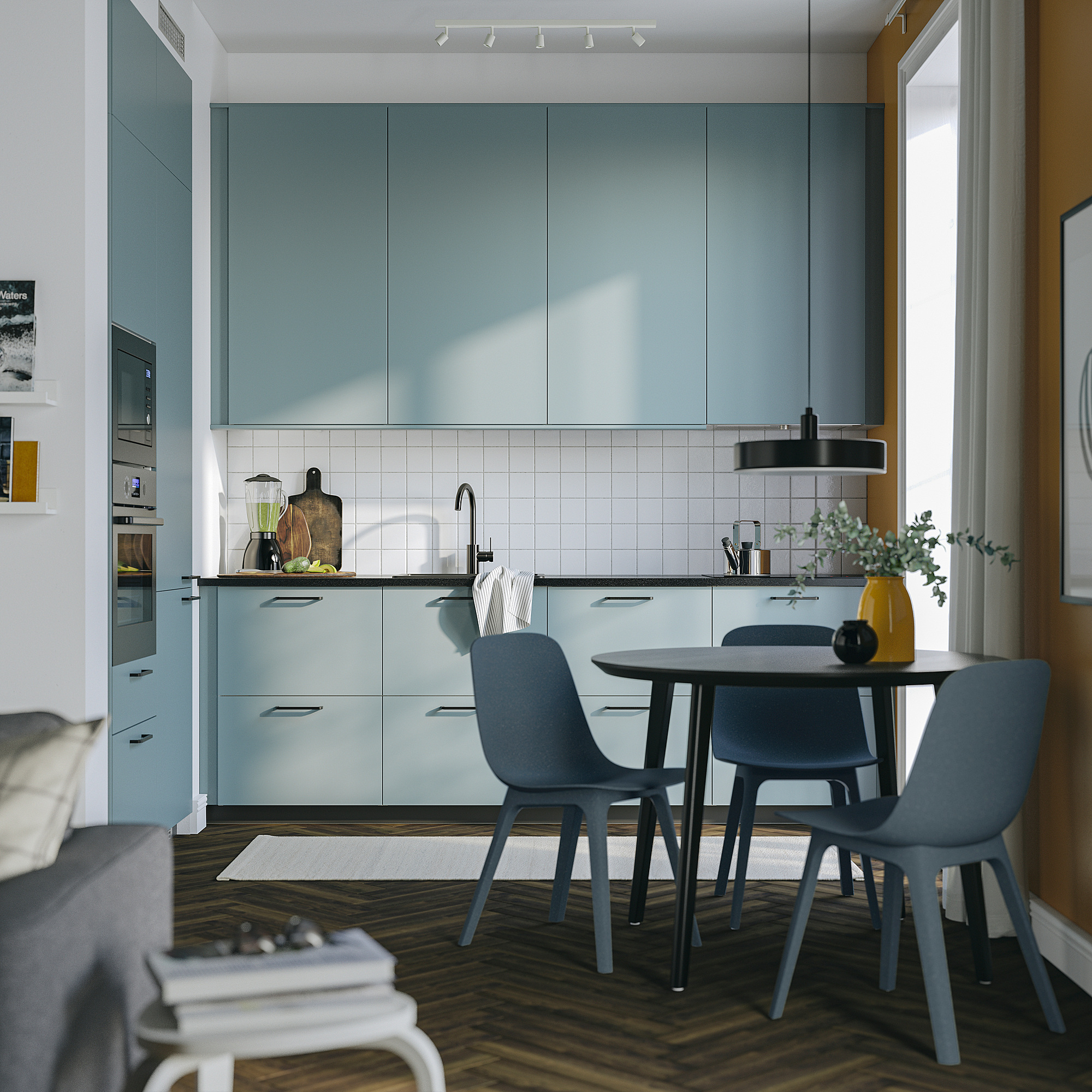 Small modern turquoise kitchen with sleek cabinets, dark wood floor, round table, grey chairs, and hanging light.