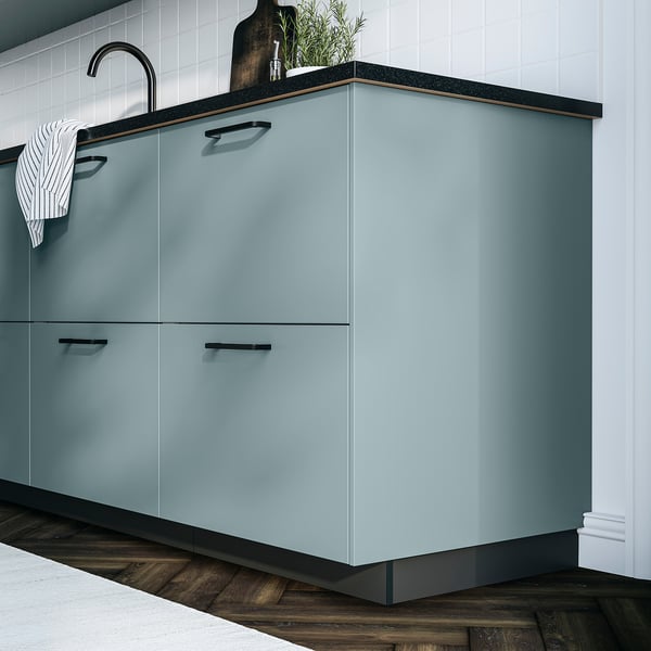 Turquoise HAVSTORP cabinet with sleek lines, dark countertop, striped towel, white backsplash, wooden floor.