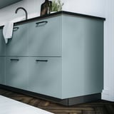 Turquoise HAVSTORP cabinet with sleek lines, dark countertop, striped towel, white backsplash, wooden floor.