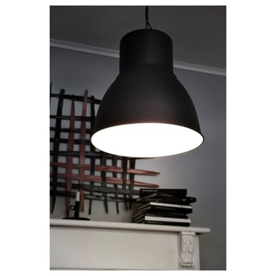 Large black pendant lamp hanging from ceiling, illuminating downward. Positioned over a white mantelpiece with stacked books and decorative lattice.
