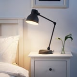 Modern HEKTAR lamp in black, adjusts to light book, rustic-contemporary design on nightstand with flowers.