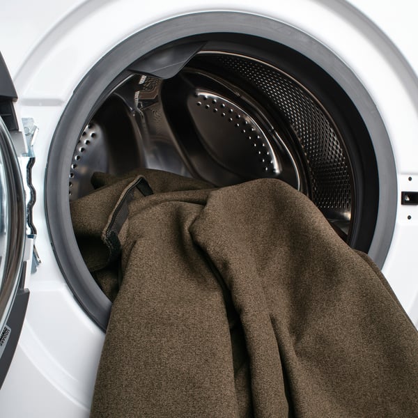 Image shows an open washing machine with a brown blanket and black clothes inside.