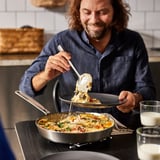 A man serves food from a stainless steel frying pan onto a plate, showcasing its easy stirring design and durability.