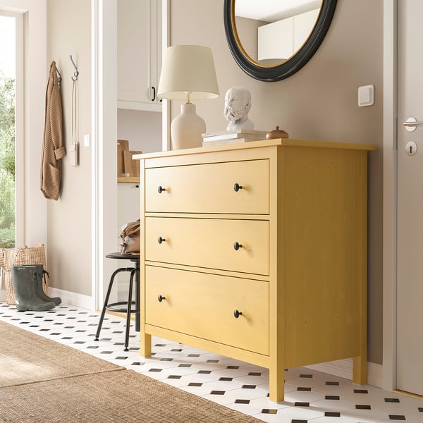 Bright yellow HEMNES chest with three drawers stands near a door, contrasting with white walls and patterned floor.