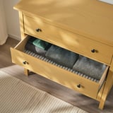 Yellow wooden chest with three open drawers, filled with folded blankets and clothes. Soft-close drawers, wall anchoring safety feature.
