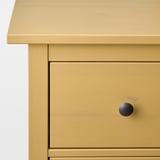 A close-up of a well-crafted mustard-yellow dresser with sleek drawer and knobs.