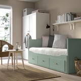 Modern small bedroom with HEMNES green day-bed, white wardrobe, and round table. Cozy, minimalist decor with soft lighting.