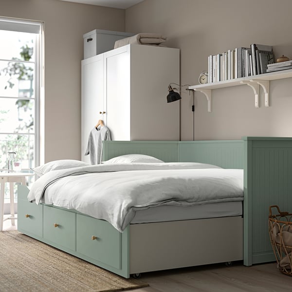 HEMNES day-bed with drawers, white pillows. White cabinet with books, lamp, and window.