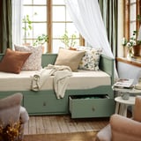 HEMNES day-bed in grey-green, sofa/bed with storage, pillows, blanket, plant, cup.