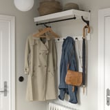 HEMNES coat rack in white, holding beige coat, blue jacket, brown bag, umbrella, wicker items, and extra hook. Fits between doors.