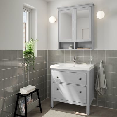 Modern gray bathroom with HEMNES vanity, white sink, large mirror cabinet, round lights, black stool with towels, and tiled walls.