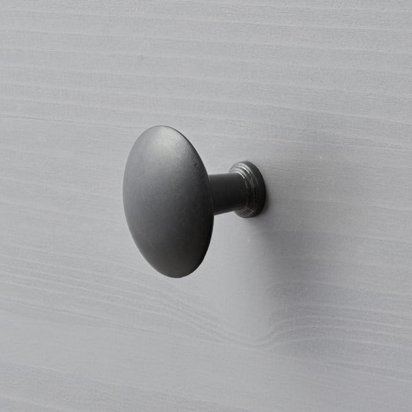 Dark, matte round wall-mounted hook on a grey wall. Minimalist design.