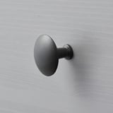 Dark, matte round wall-mounted hook on a grey wall. Minimalist design.