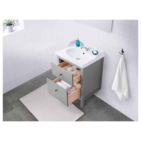 Clean, modern bathroom vanity with grey cabinet, open drawers, white sink, and accessories.