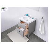 Clean, modern bathroom vanity with grey cabinet, open drawers, white sink, and accessories.