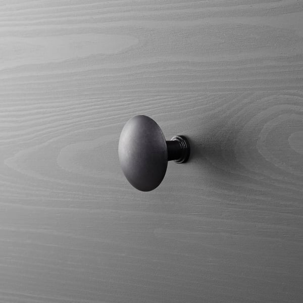 Dark metal wall-mounted hook on gray wooden surface.