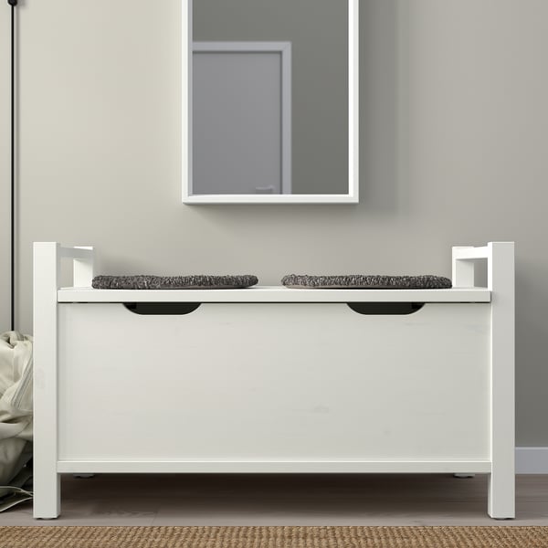 White wooden HEMNES bench with two open shelves for storage, placed against wall with mirror.