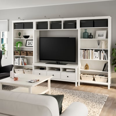 Modern living room with white HEMNES entertainment center, tv, books, and decor. Cozy sofa on rug, plants, and coffee table.