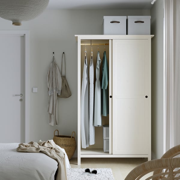 Bedroom with white HEMNES wardrobe, sliding doors open showing clothes and shelves. Clothes hangers, baskets below.