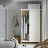 Bedroom with white HEMNES wardrobe, sliding doors open showing clothes and shelves. Clothes hangers, baskets below.