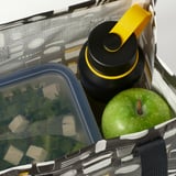 Open lunch bag reveals an insulated water bottle, a green apple, and a container of cheese cubes and greens, all packed neatly for a meal on the go.