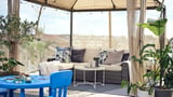 Beige wicker loveseat, dark cushions, white & blue tables, plants, gazebo with lights.