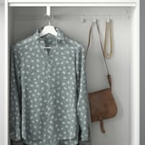 Hanging gray polka-dot shirt with white hanger in closet, leather bag, and gold necklace on hooks.
