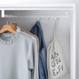 White clothes rail in shallow closet; holds several hanging garments, including a grey sweater and blue jacket.