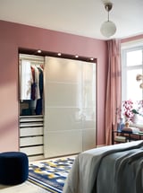 Bedroom with HOKKSUND pinkish wardrobe, mirrored doors. Bed with gray blankets, divine rug, round blue stool.
