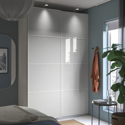 Modern bedroom featuring HOKKSUND high-gloss gray wardrobe with sliding doors, accompanied by a bed, plant, and mirror.