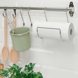 Metal rail with hooks holds green cup and paper towel for kitchen storage.