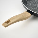 Close-up of non-stick frying pan with wooden handle on white surface.