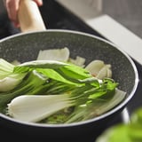 Cooking black pan with green vegetable, likely pak choi, ensuring even heat and easy cleaning.