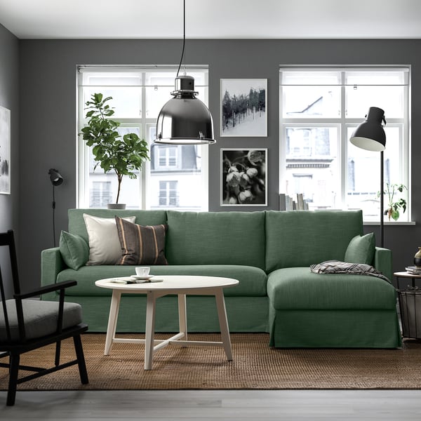 Modern living room with gray walls, green l-sofa, coffee table, lamps, plants, art.