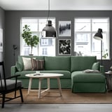 Modern living room with gray walls, green l-sofa, coffee table, lamps, plants, art.