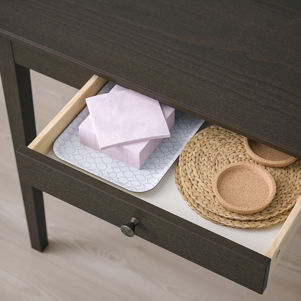 Open dark wood desk drawer showing organized items: pink napkins and woven baskets on a patterned liner.