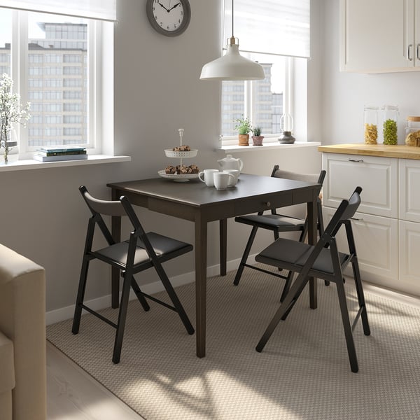 Modern dining setup with IDANÄS table & chairs, city view. Table has drawer & foldable leaf, fits elegantly in room with white decor.